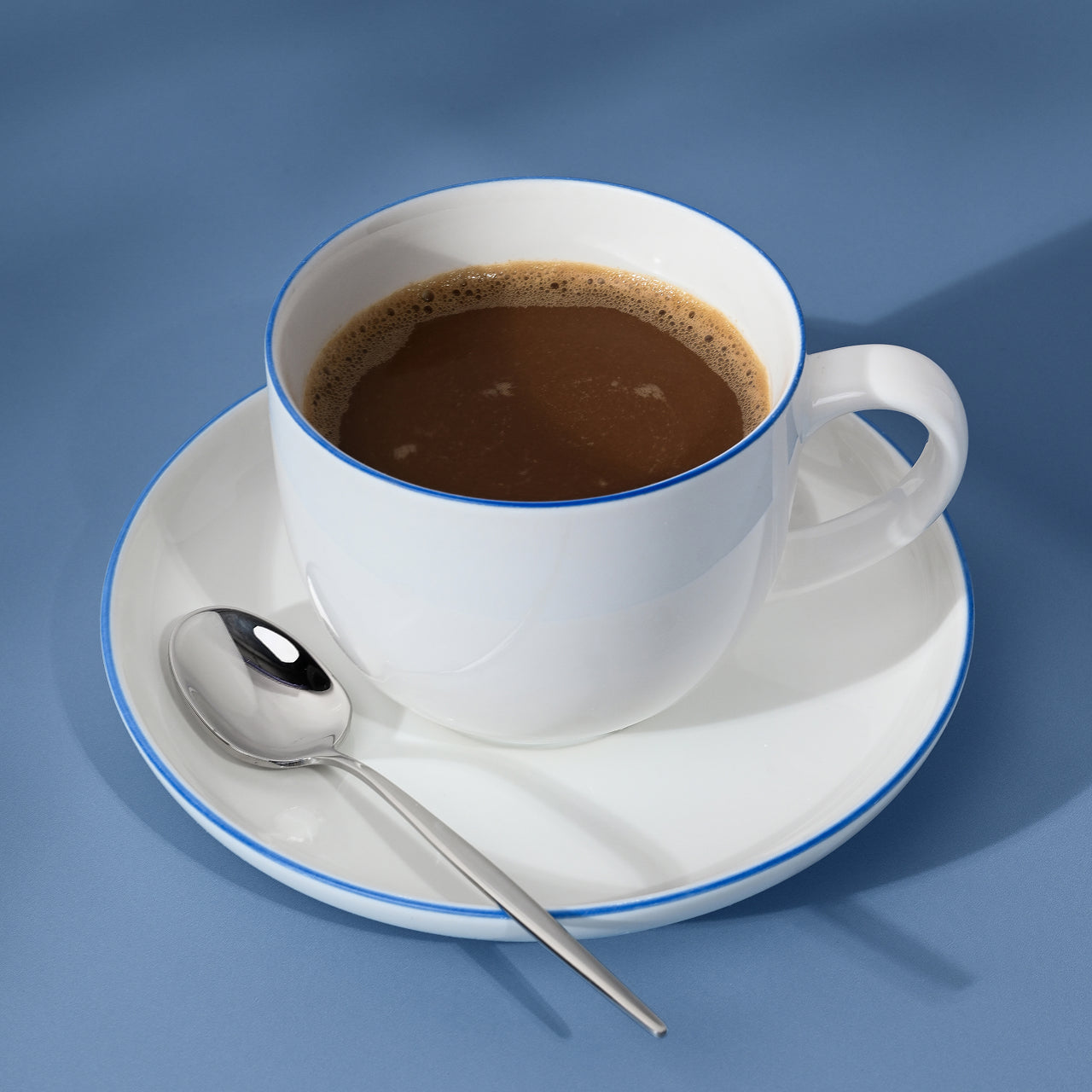 White cup of coffee on a saucer with a spoon, blue background.